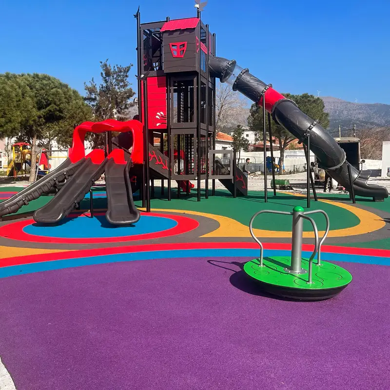 Gri ve kırmızı oyun kulesi ile mor, mavi ve kırmızı dökme kauçuk zemin uygulanmış park