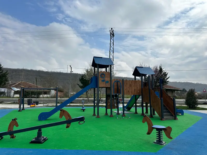 Ahşap oyun kulesi, kaydırak ve zıp zıp figürleriyle yeşil kauçuk zeminli park