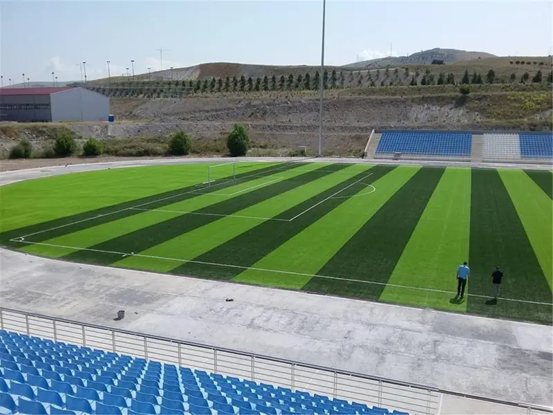 Mavi tribünlü stadyumda çizgili serilmiş suni çim saha